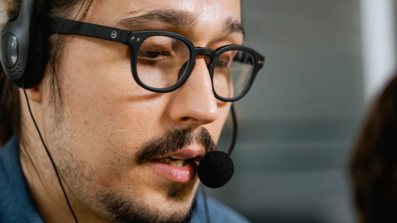 Close de um atendente de óculos usando headset durante uma ligação.