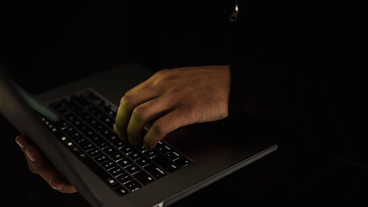 Mãos digitando num notebook no escuro, com só o teclado à vista.