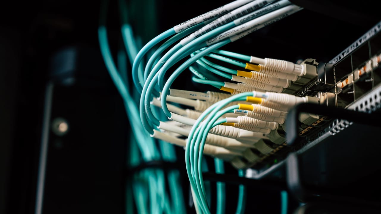 Cabos de rede de fibra conectados a um rack de servidor, em tons de ciano.