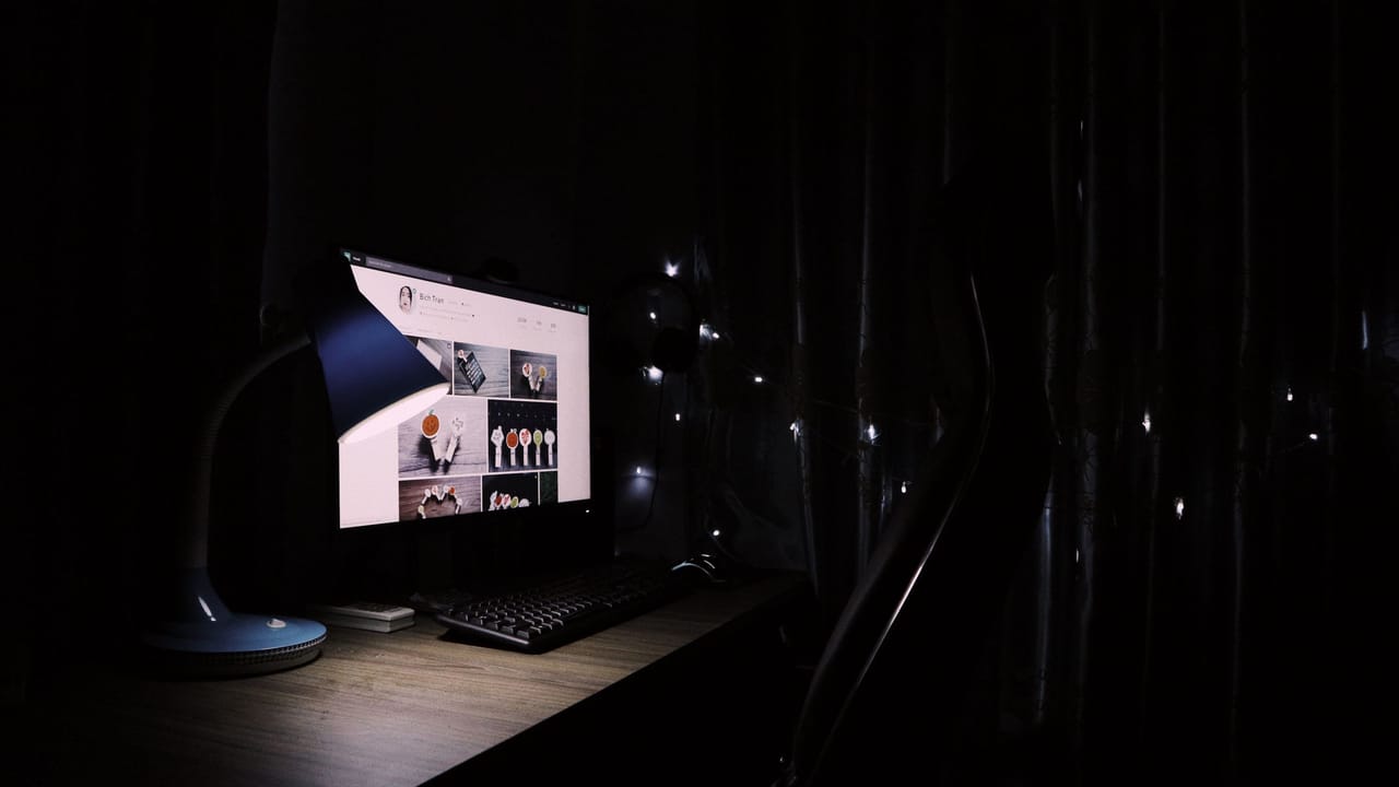 Mesa de escritório em casa à meia-luz, com um monitor aceso mostrando uma página da web.