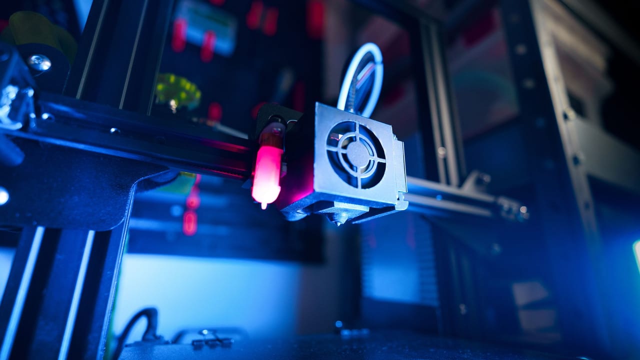 Cabeçote de uma impressora 3D em funcionamento, iluminado por luz azul.