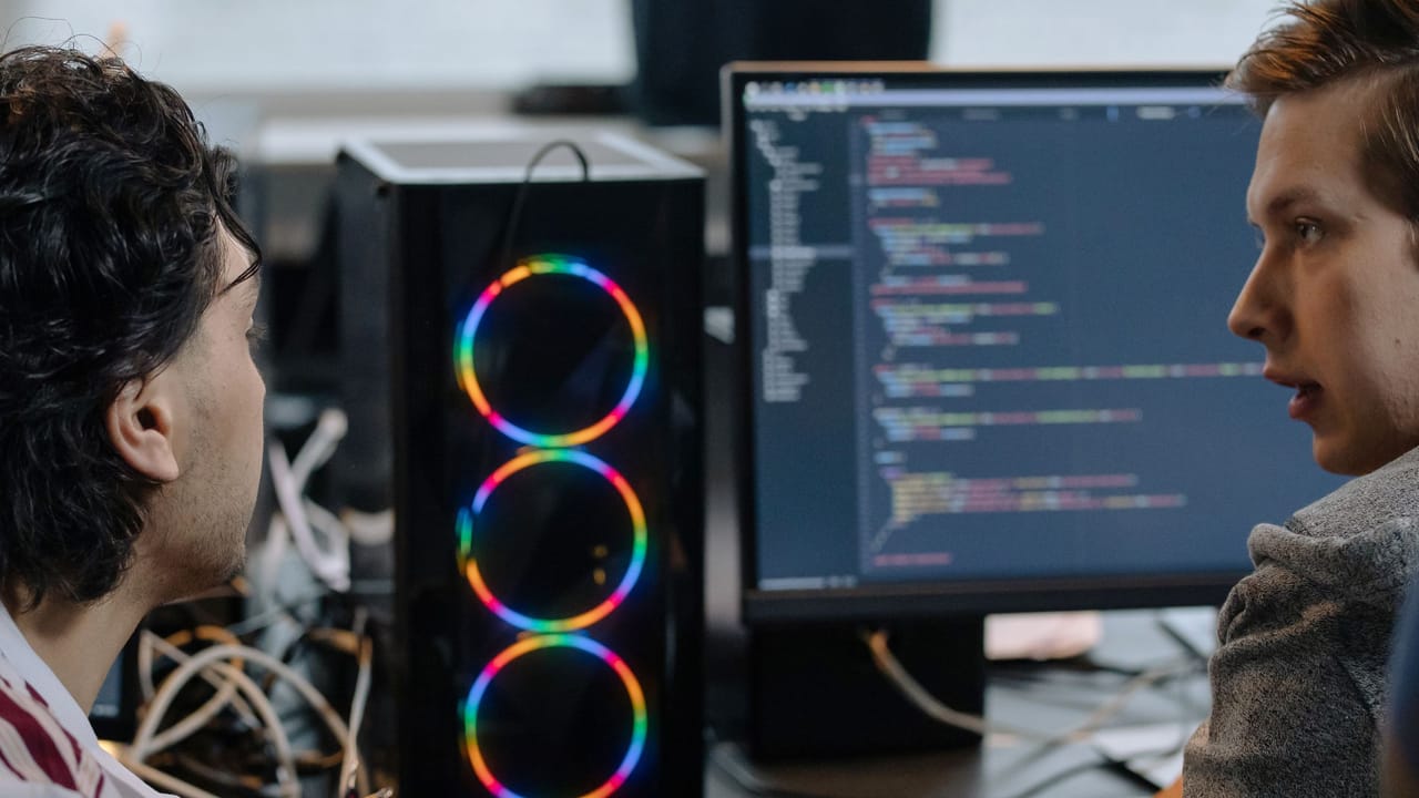 Dois programadores conversando diante de um monitor com código.